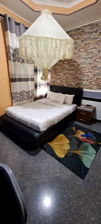 Queen bed under a white lace canopy, black headboard and a stone feature wall